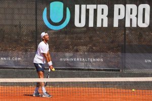 Tennis Player serving in front of UTR Banner